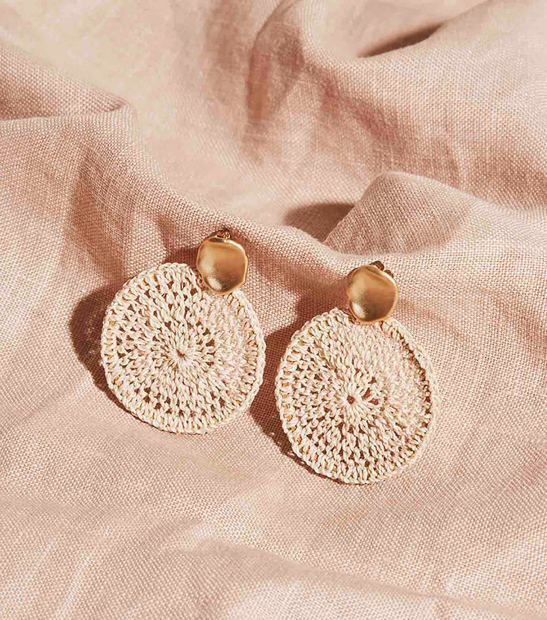 Gold disc earrings with handwoven natural fibre hoops on a white background.
