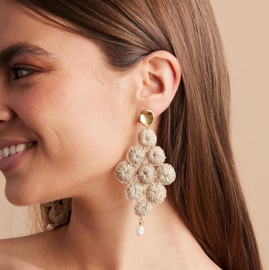 Natural fibre discs in a diamond shaped statement earring on a woman smiling