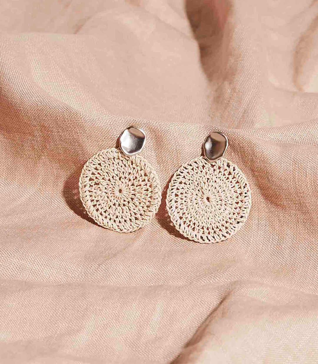 Silver earrings with handwoven natural fibre discs on a white background.