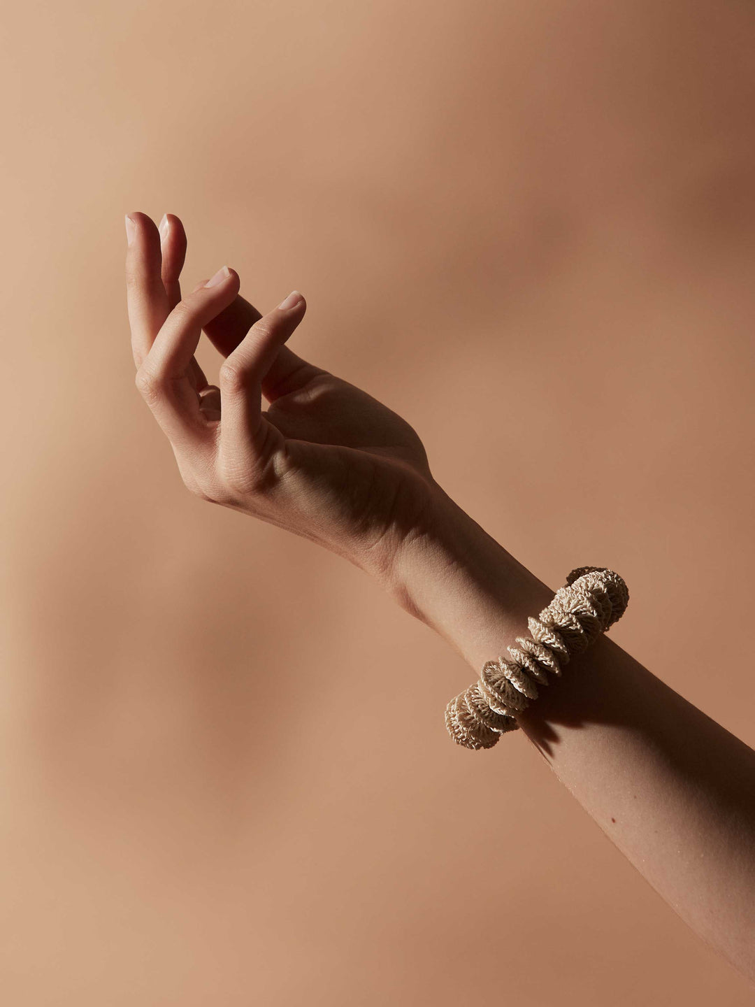 Handwoven bracelet of natural fibre beads on a models wrist against a warm brown backdrop.