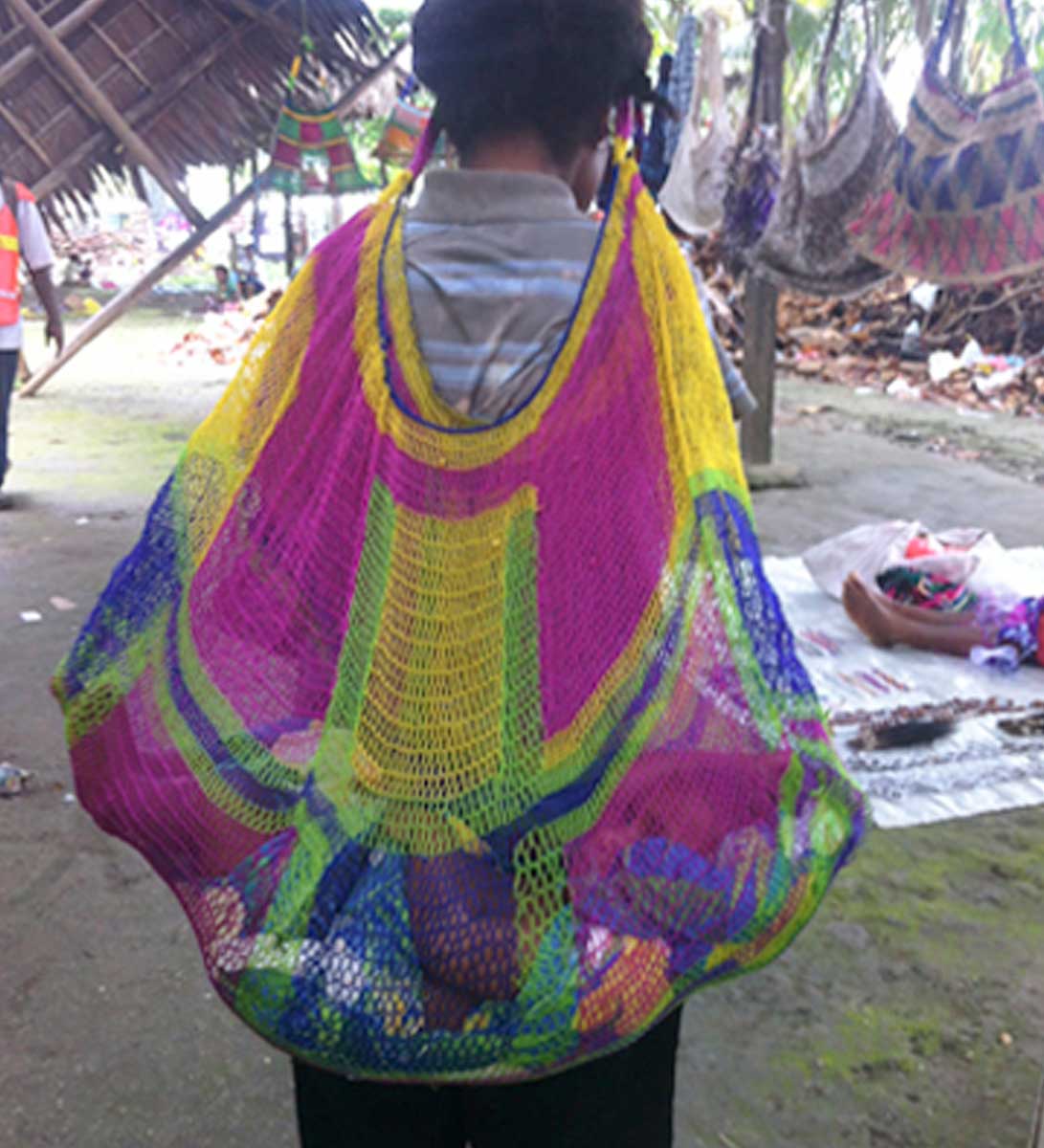 Papua New Guinean woman carrying a baby in a bilum on her head at the markets.