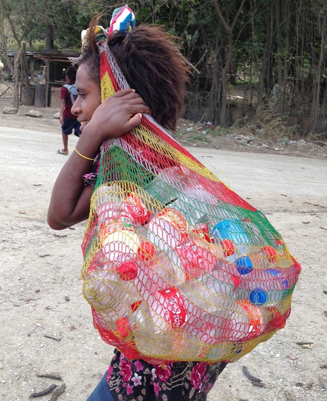 Young woman carrying ice cold water in coca cola bottles in a bilum on her head