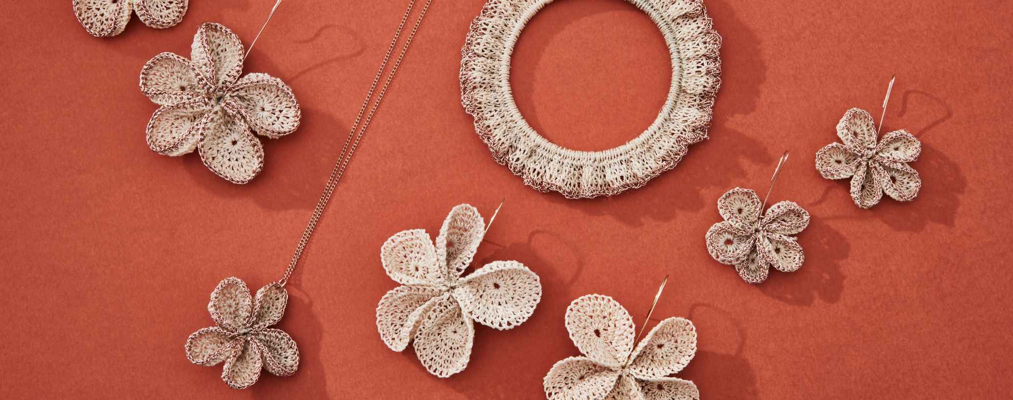 Bilum and bilas handwoven flower jewellery collection laid on a burnt orange background