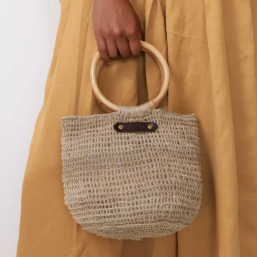 Handwoven natural fibre bucket bilum with cane handles the betty basket from Bilum and Bilas being held by a models hand