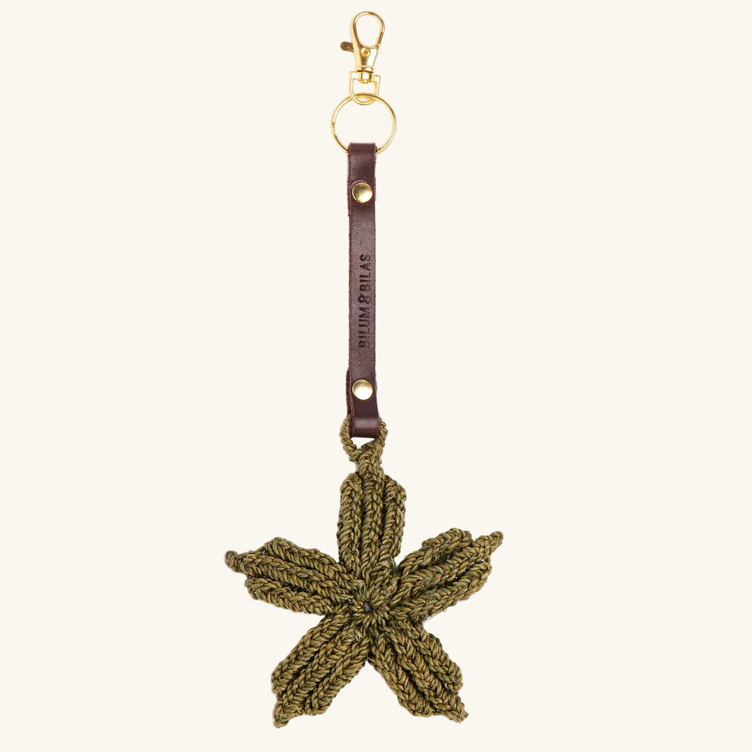 Green crocheted leaf-shaped keychain with brown leather strap on a white background