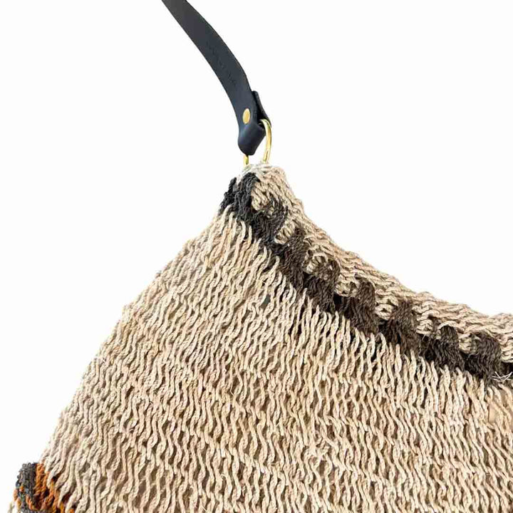 Close up on the opening and strap of a striped natural fibre bilum with leather strap.