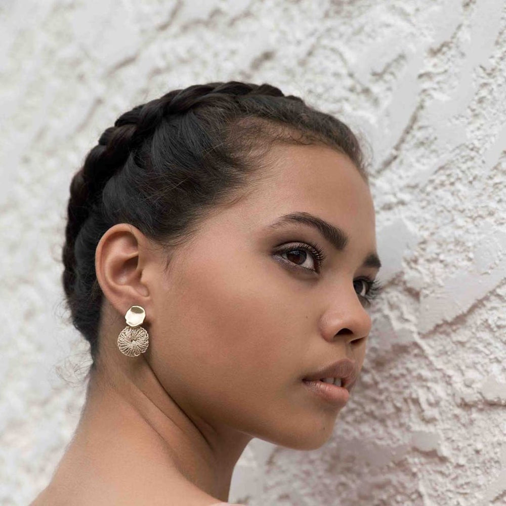 Model wearing Bilum and Bilas warped gold stud earring with a dangling handwoven natural fibre disc 