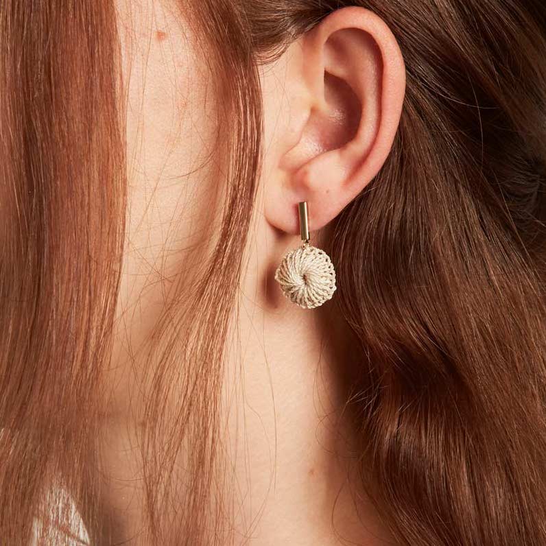 Model wearing Bilum and Bilas gold bar earring with dangling handwoven natural fibre disc