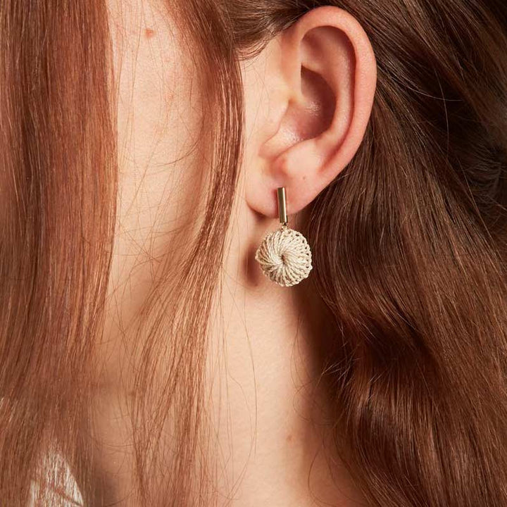 Model wearing Bilum and Bilas gold bar earring with dangling handwoven natural fibre disc 