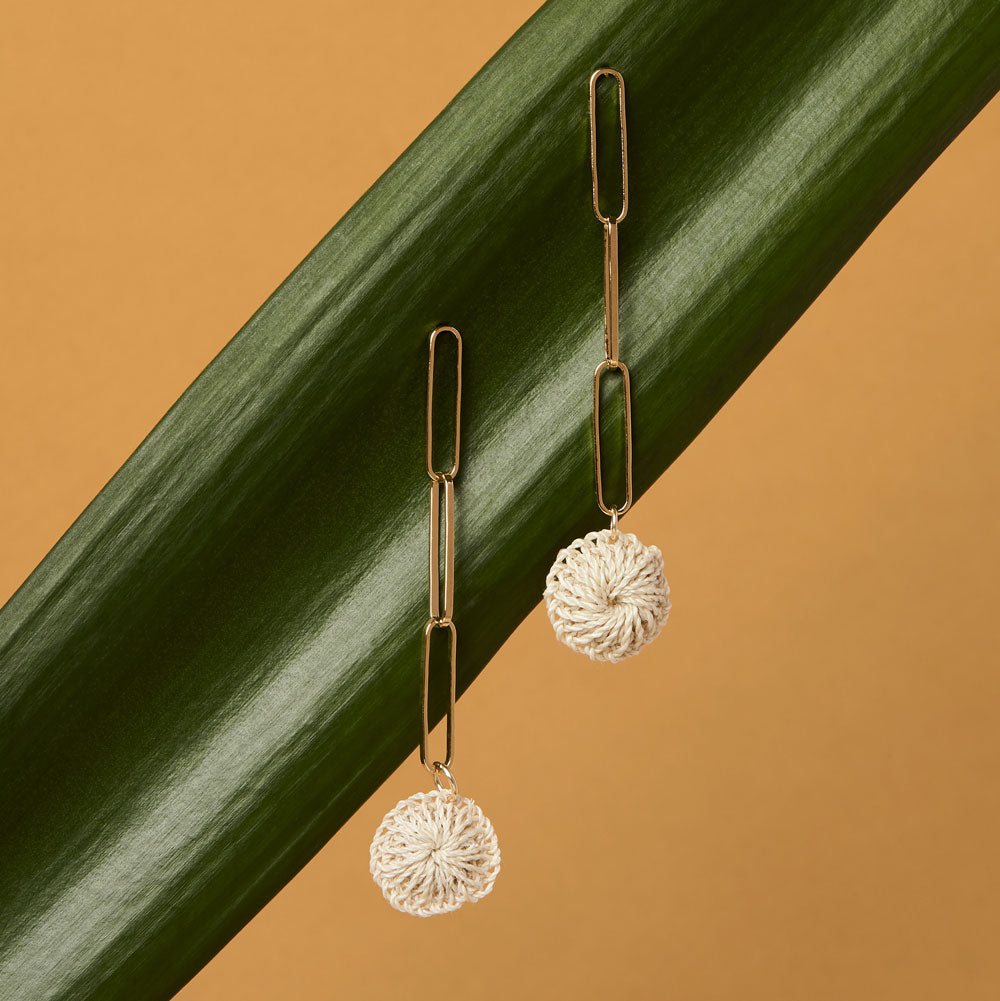 Gold paperclip chain dangle earrings with natural fibre woven disc on a leaf still life