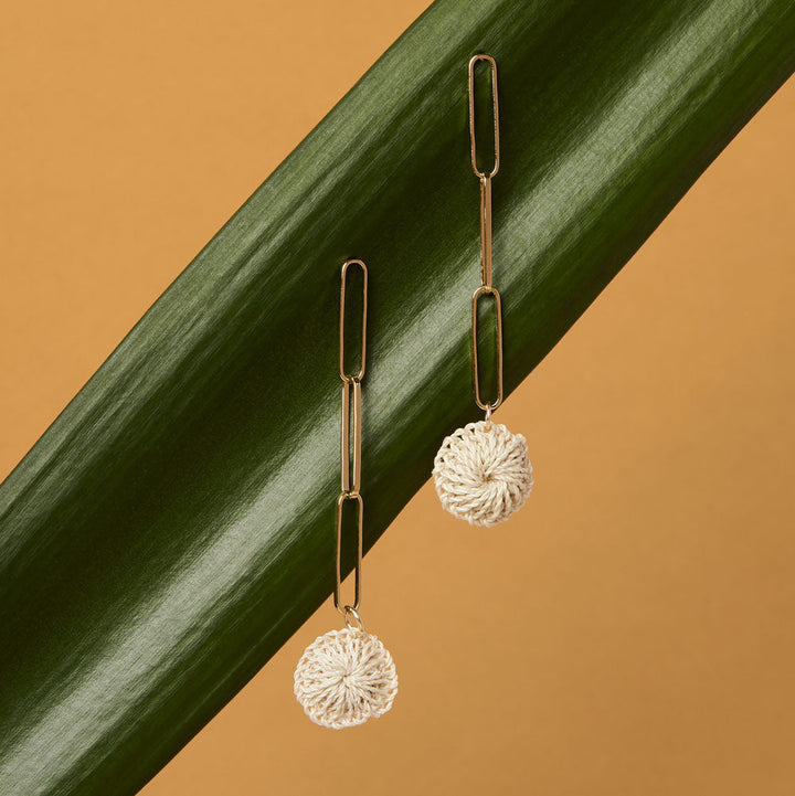 Gold paperclip chain dangle earrings with natural fibre woven disc on a leaf still life