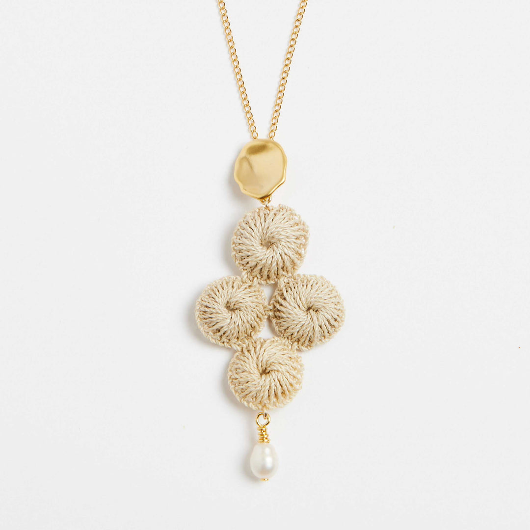 Close up of gold filled chain necklace with pearl and woven natural fibre pendant