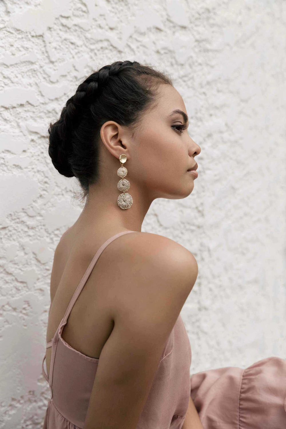 Model in pink dress wearing Bilum and Bilas sowana droplet earrings with warped gold earring and a tri of dangling natural fibre discs