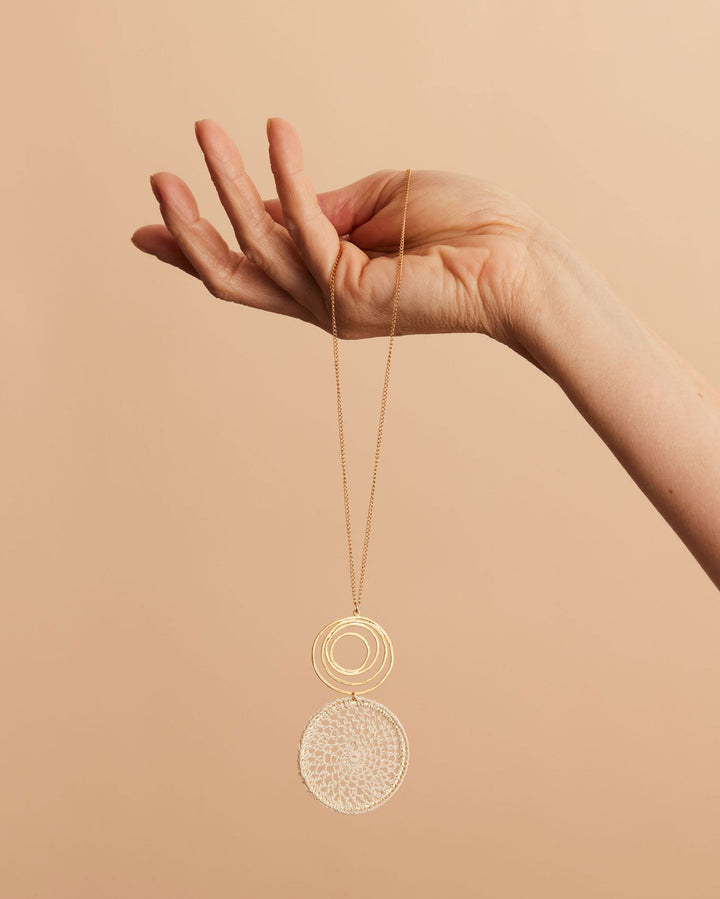 Hand still life holding gold filled fine chain necklace with gold swirl and natural fibre woven disc pendant and matching earrings