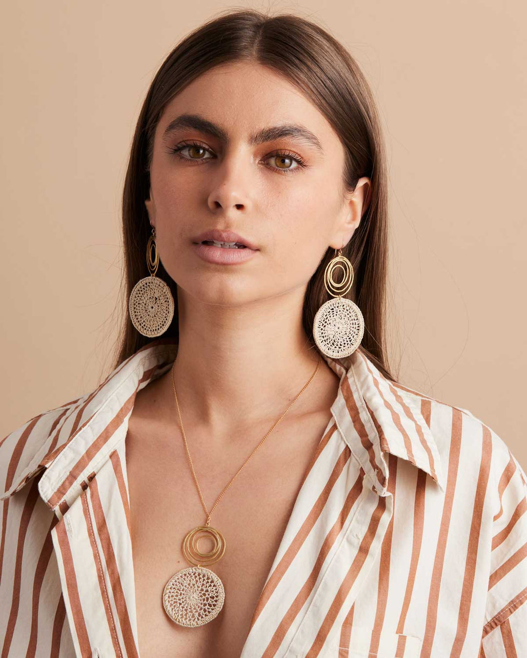 Model wearing gold filled fine chain necklace with gold swirl and natural fibre woven disc pendant and matching earrings