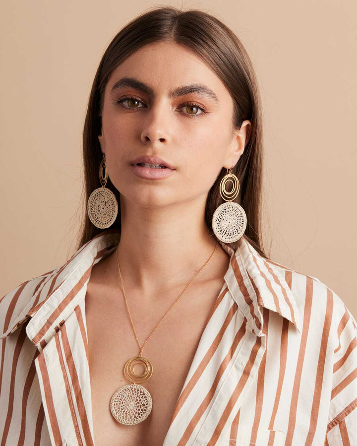 Model wearing dangling gold swirl earrings with natural fibre woven disc and matching necklace in a stripy shirt