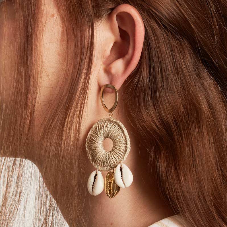Model wearing a Dangle statement gold earring with handwoven hoop featuring natural and gold cowry shells
