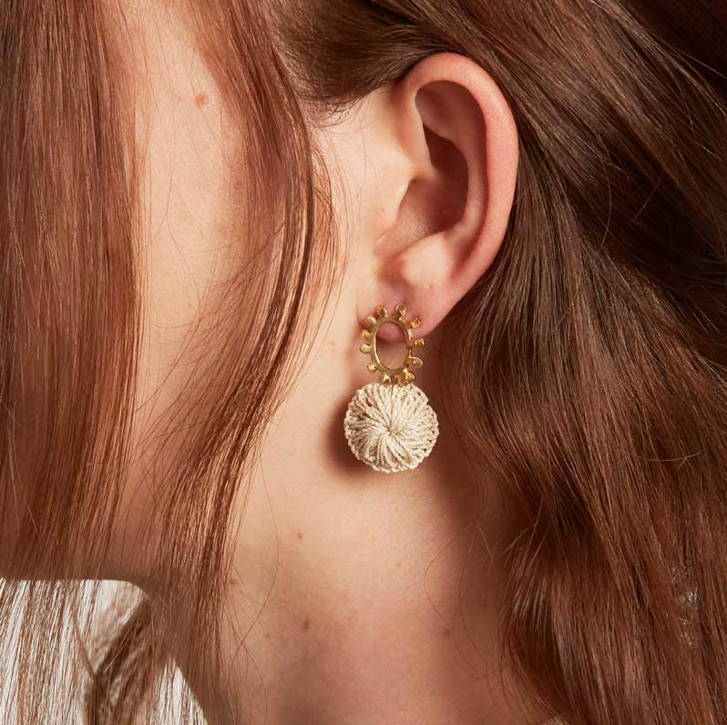 Model profile wearing gold textured sun earrings with natural fibre woven discs
