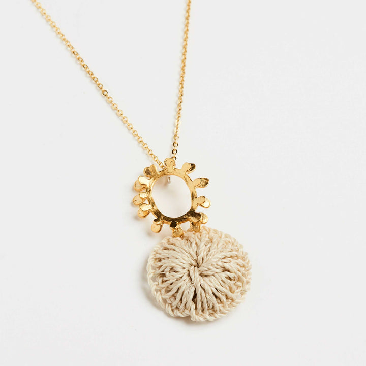 Angled close up of gold textured sun pendant with natural fibre woven disc on a gold filled chain necklace