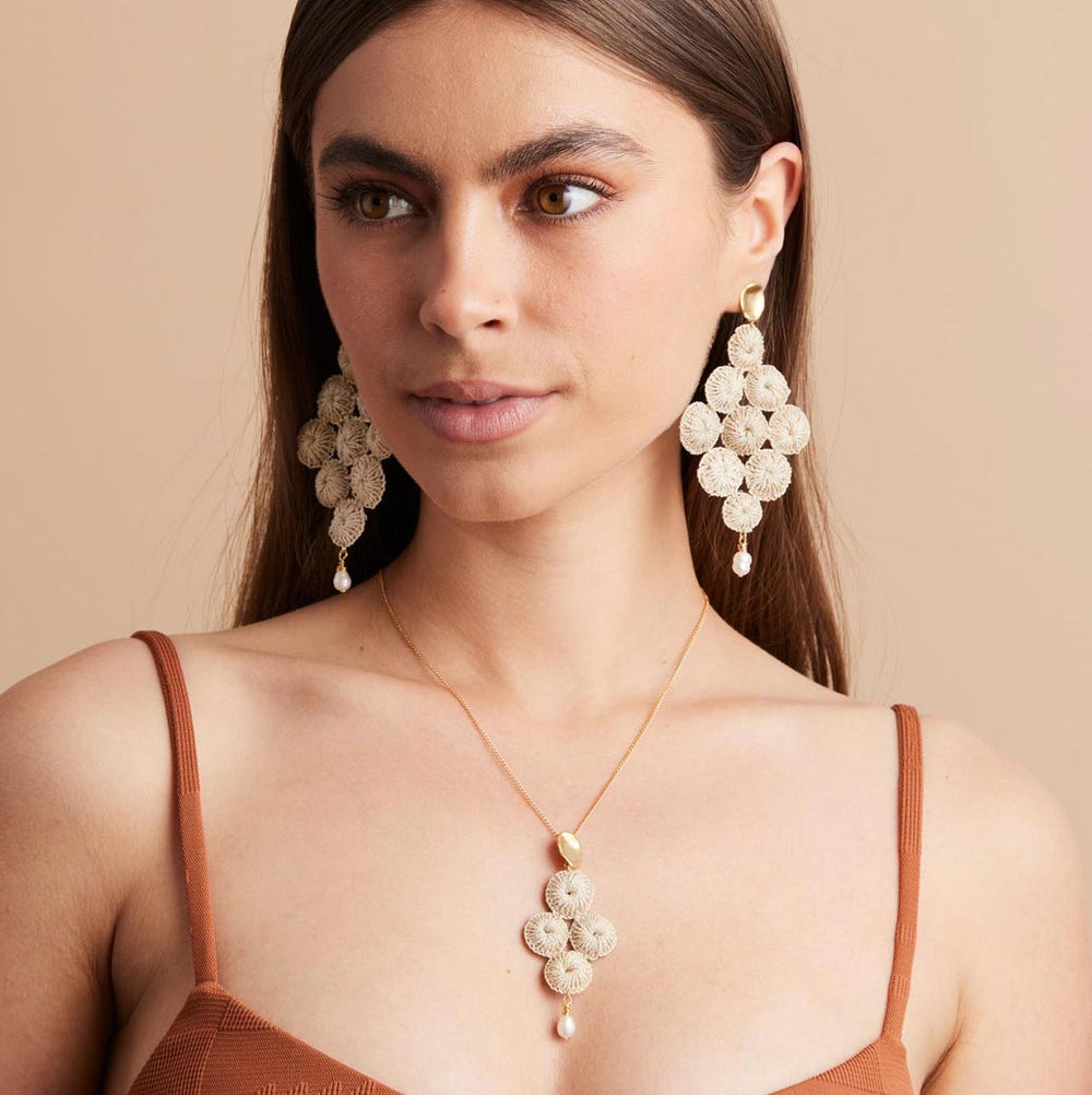 Gold filled chain necklace with pearl and woven natural fibre pendant on model glancing sideways