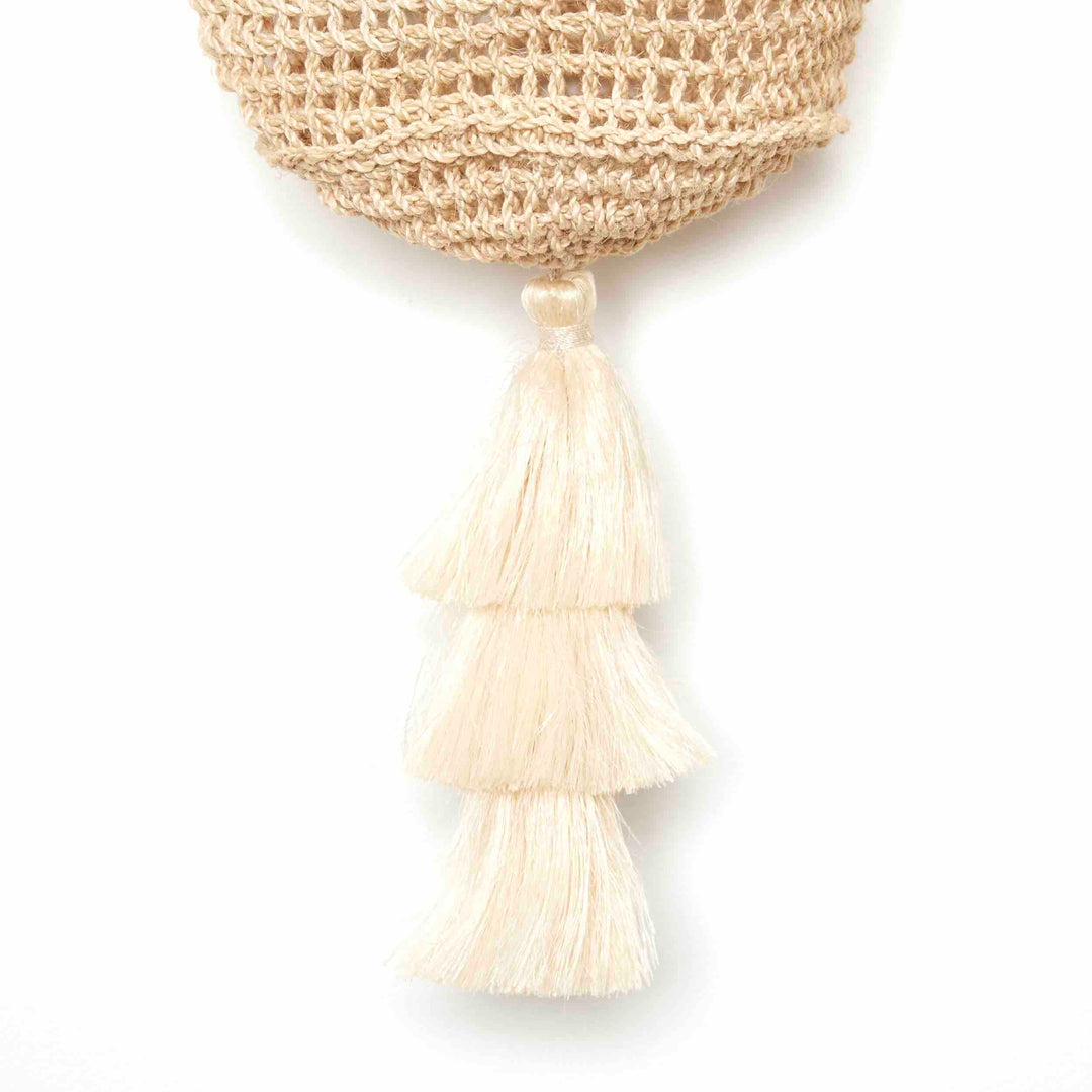 Close up on tassel on the base of a natural fibre woven bucket bag.