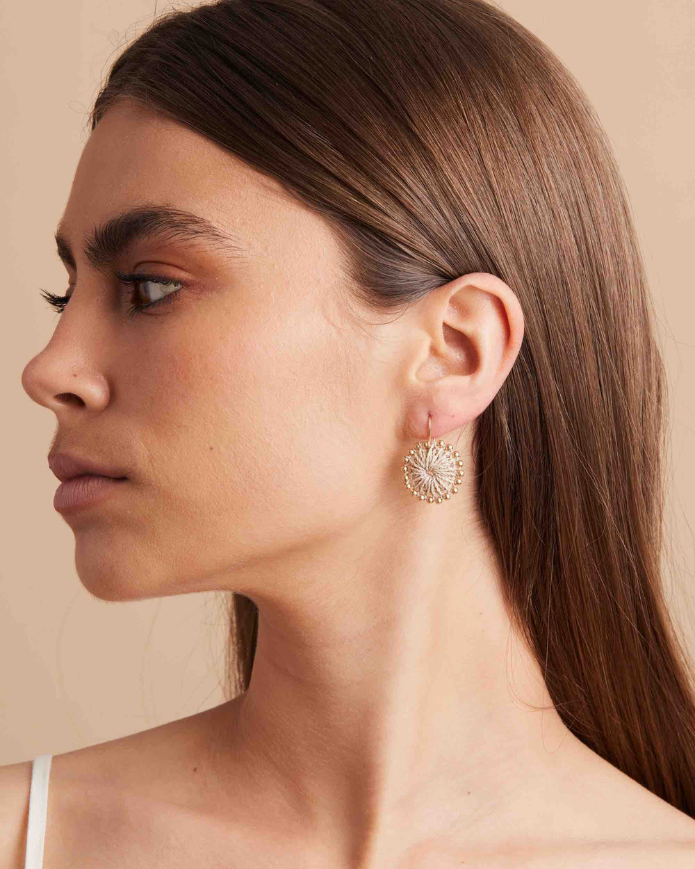 Model side profile wearing gold beaded natural woven earring and matching bangles
