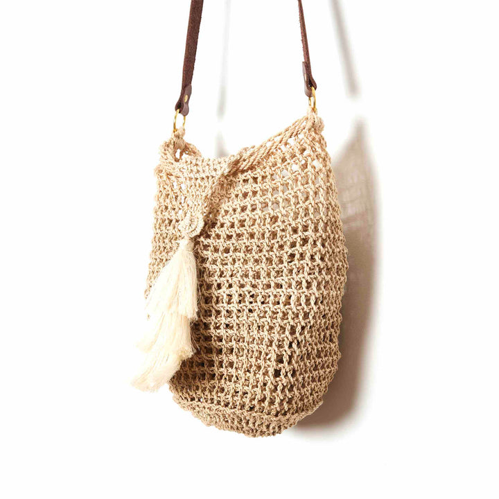 Side angle of natural fibre bucket bilum with lid close and tassel hanging on a white background.