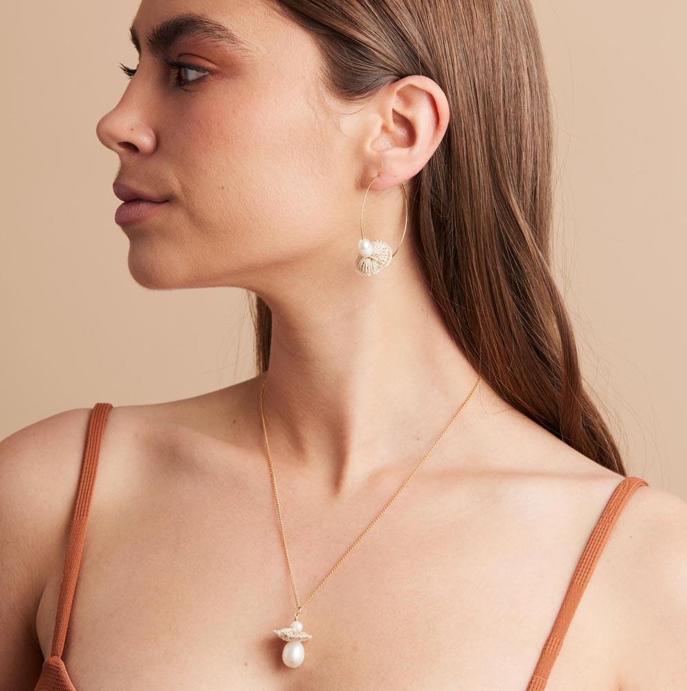 Model wearing large gold hoops with pearl and woven natural fibre discs