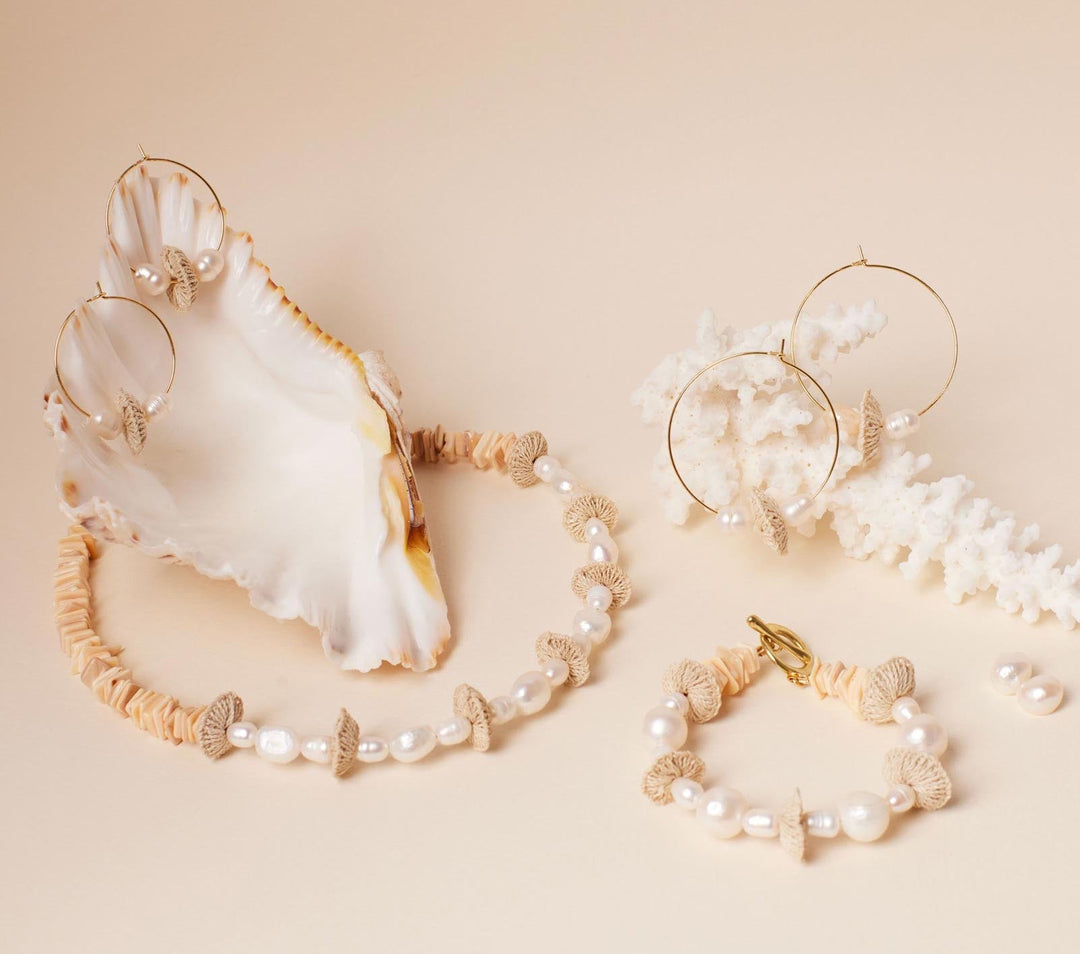 Still life with coral and shell featuring gold hoops with pearl and natural fibre discs