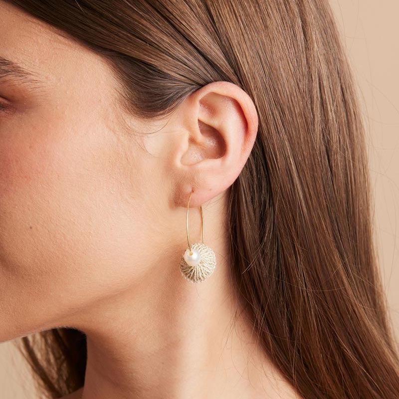 Side profile of model wearing gold hoops with pearl and natural fibre discs