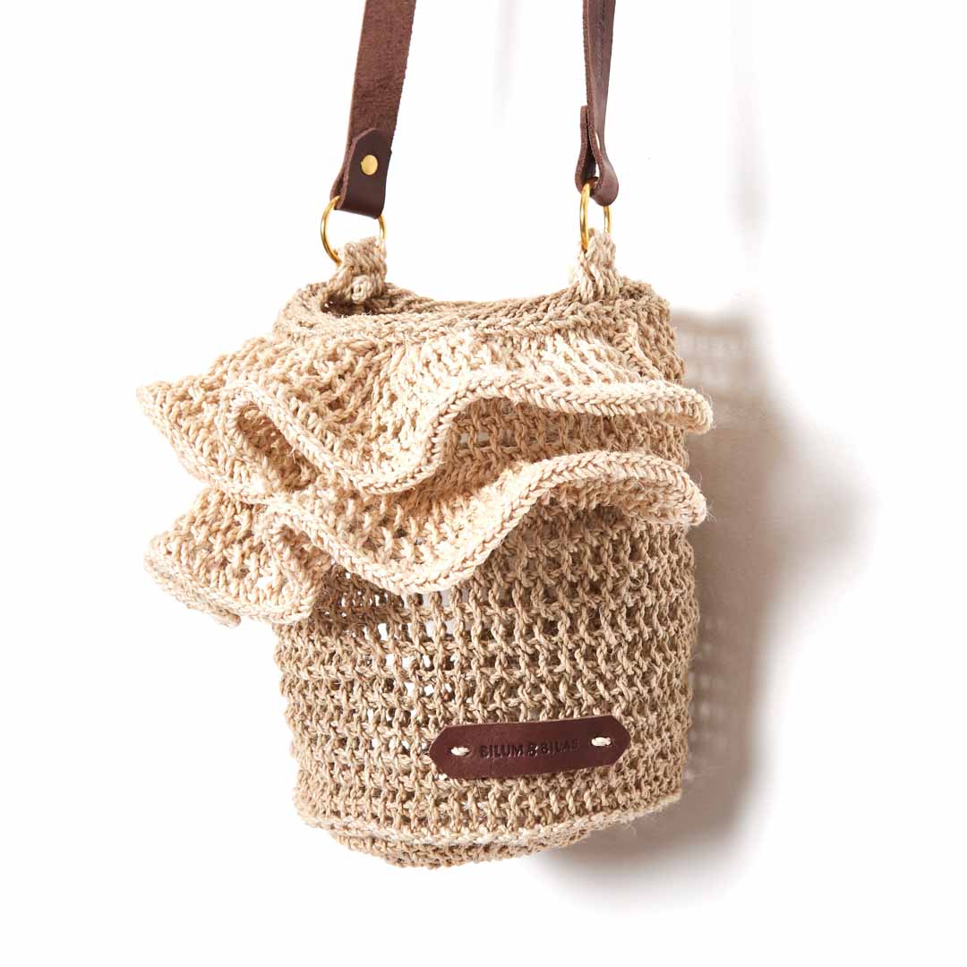 Ripple cross body bag with woven ruffle trims hanging on a side angle.