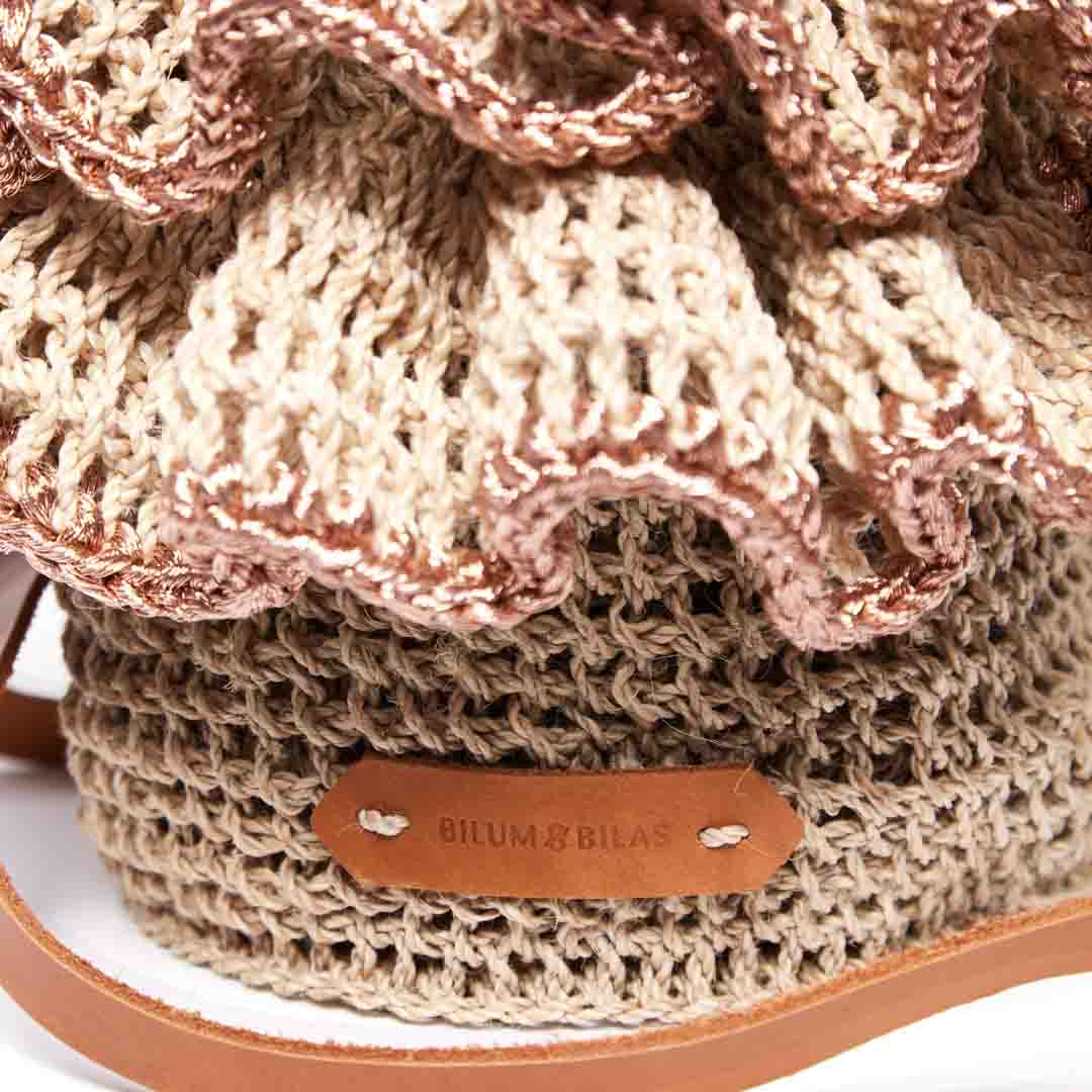 Detail on logo of the Ripple Cross Body Bag with woven ruffles with rose gold metallic trims.