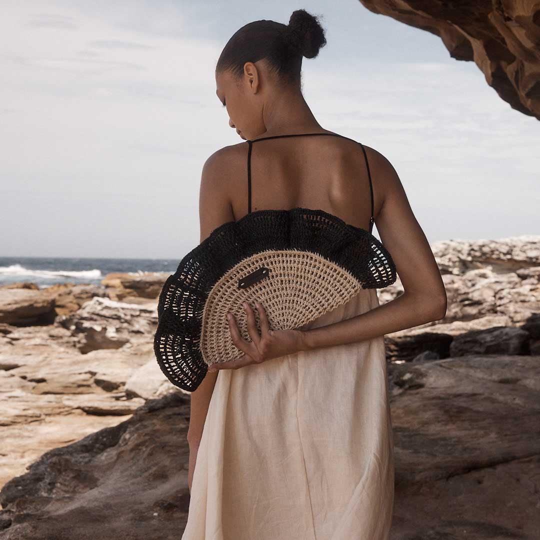 Close up of model on rocks holding the Black Ripple Clutch bag.