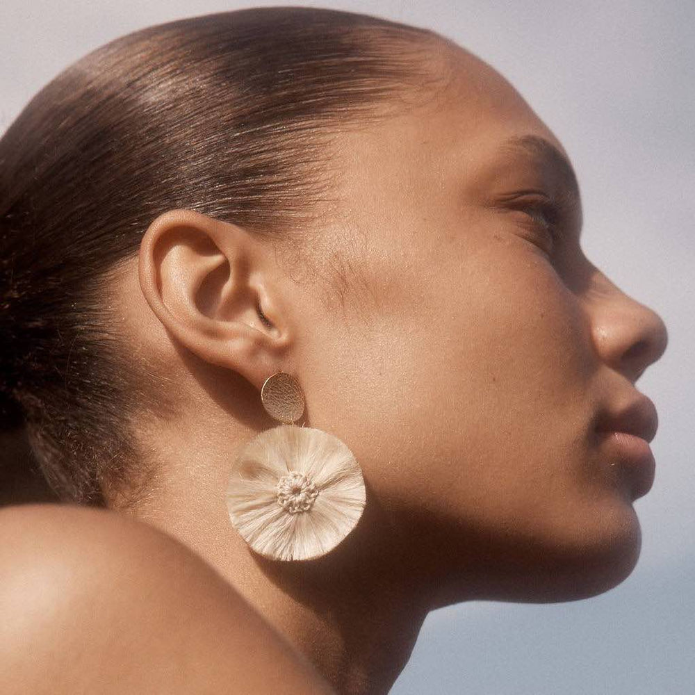 Natural fibre and gold disc pom pom earrings on a model. bilum and bilas