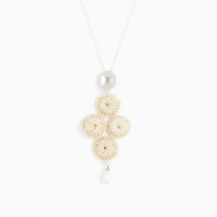 Close up of sterling silver chain necklace with pearl and woven natural fibre pendant
