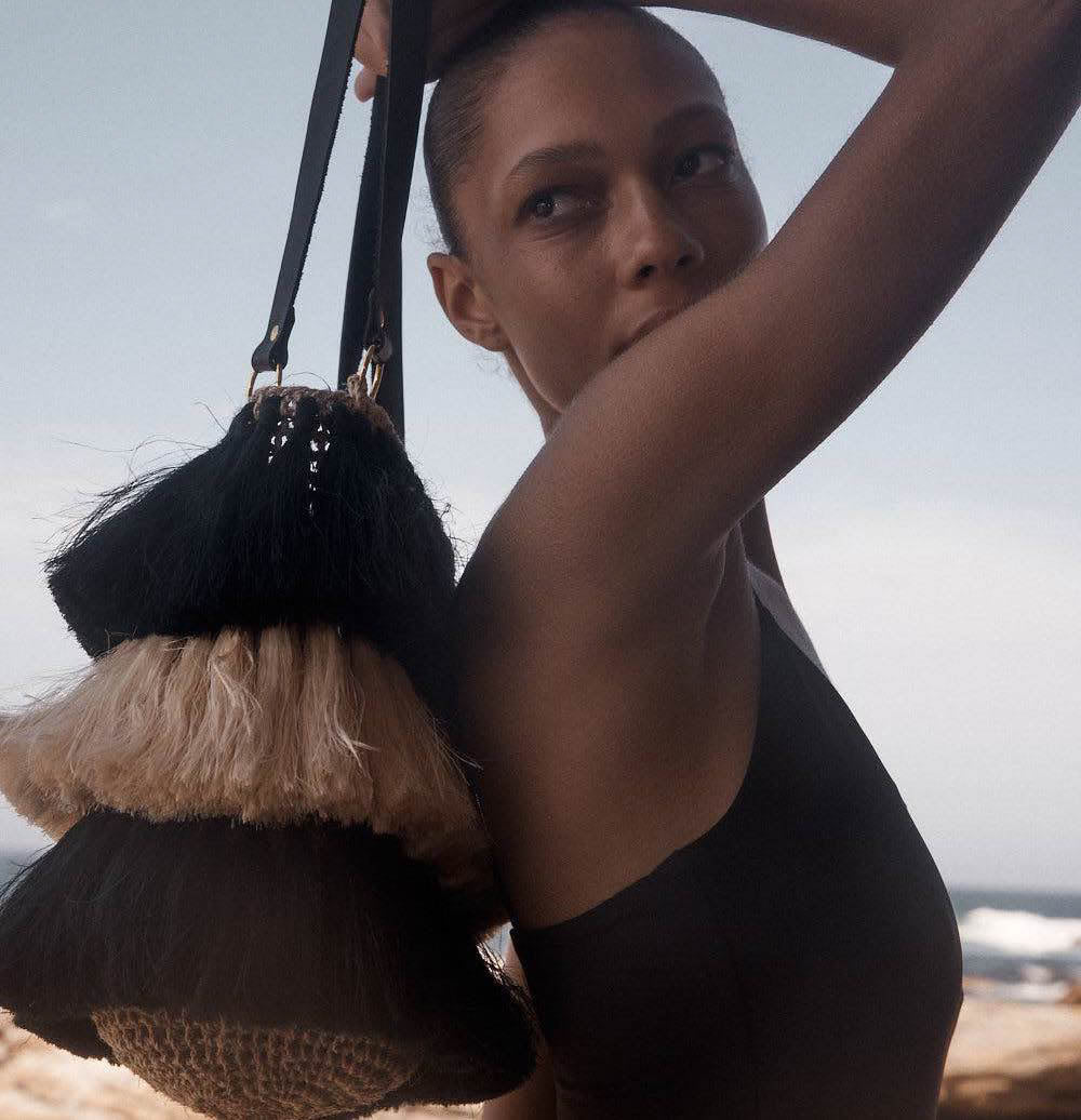 Model holding Black and white handwoven tassel bag on rocks.
