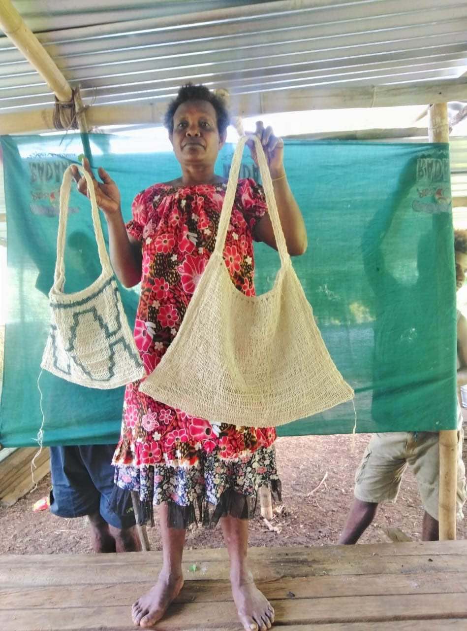 Papua New Guinean weaver Susan Alok holding up string bilums that she has handwoven