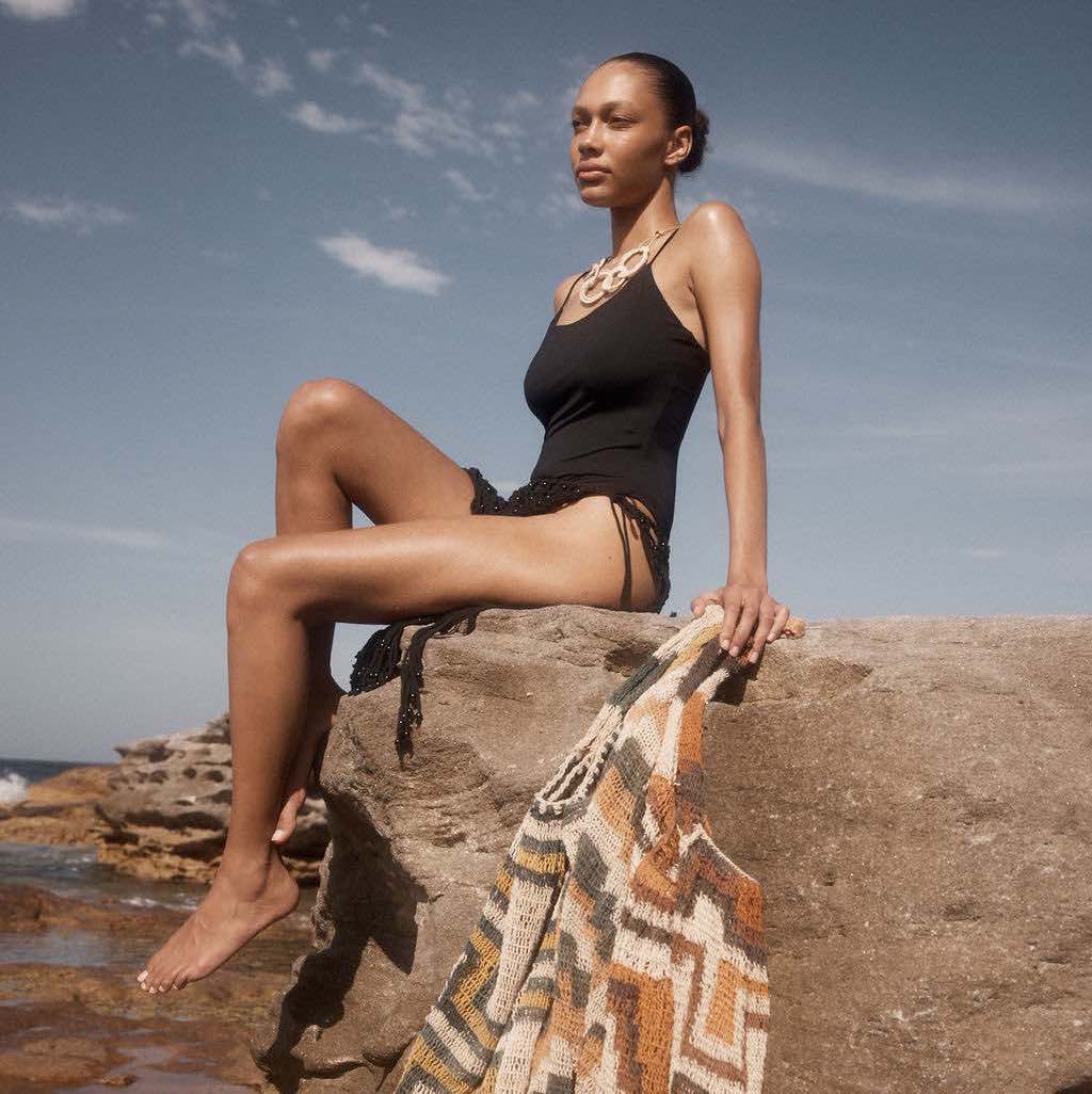 Model wearing woven chain necklace sitting on a rock.