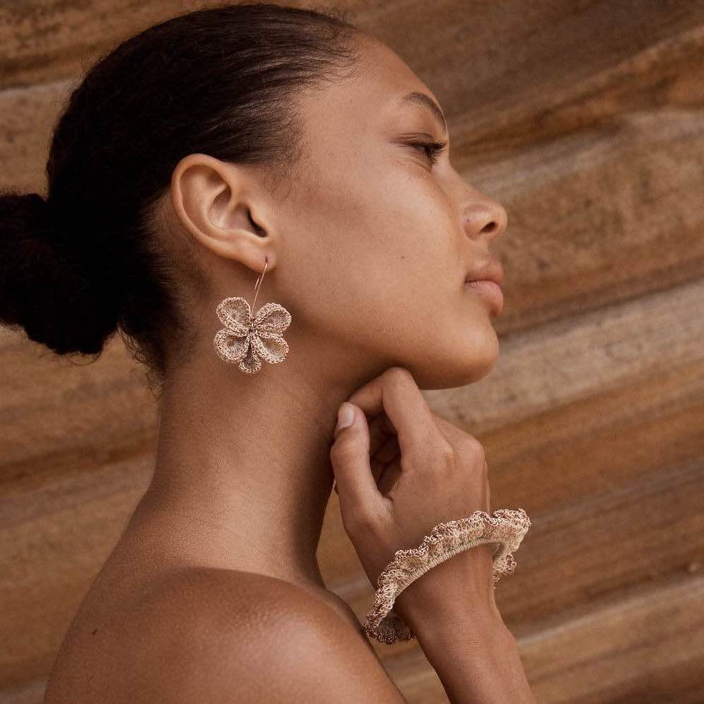 Natural fibre and rose gold metallic ruffle bracelet on model next to rocks.