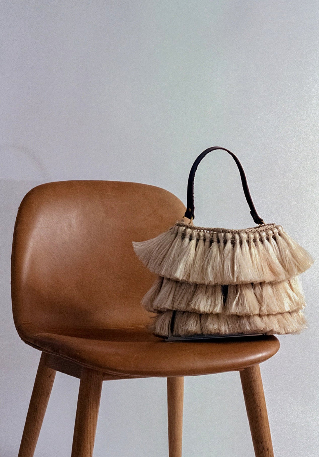 Handwoven tassel bag made from natural fibre on a burnt orange leather chair still life composition.