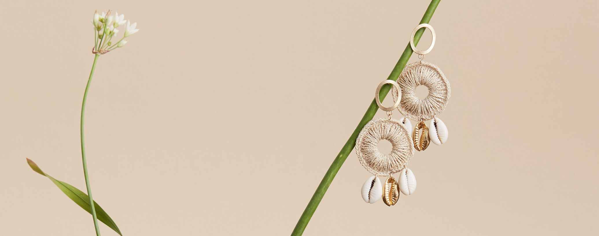 Cowry shell tropical statement earrings by bilum and bilas hanging in a still life on a flower stem