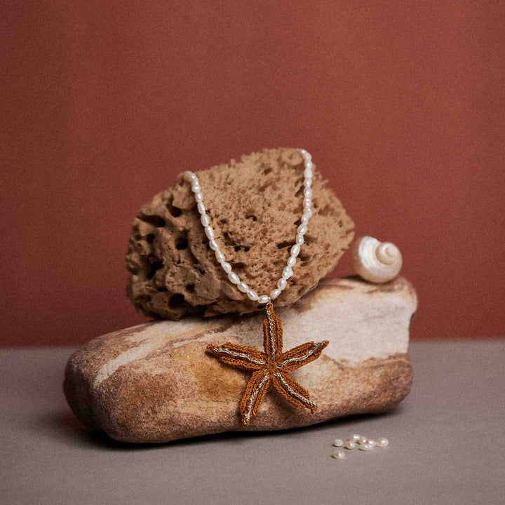 Starfish pendant necklace on a rock with a shell against a brown background