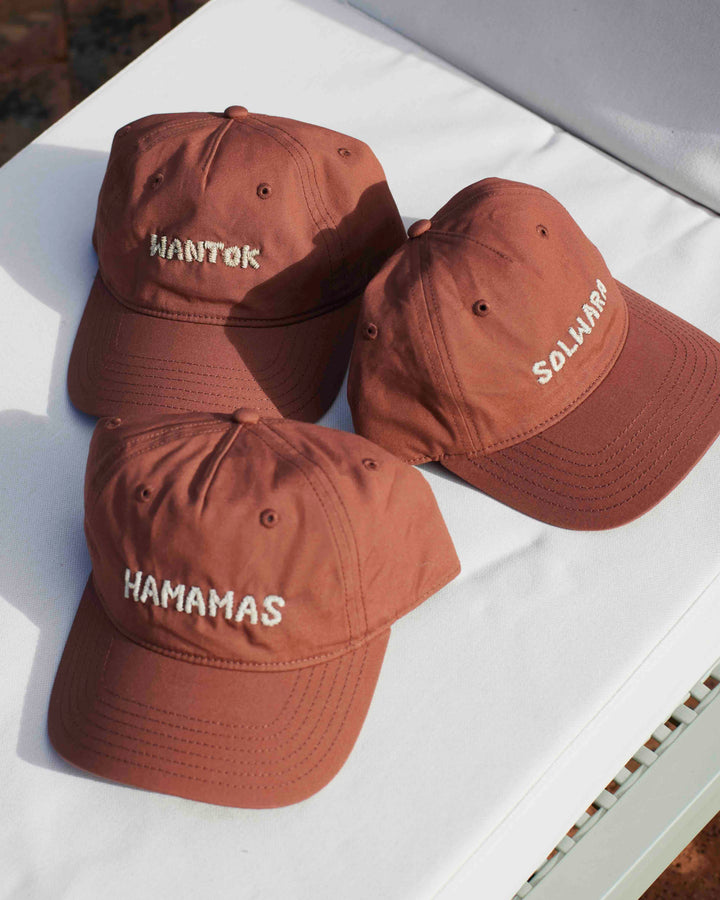 Three brown baseball caps with white embroidered text reading 'HAMAMAS', 'SOLARAY', and 'HANTOK' arranged on a white surface.