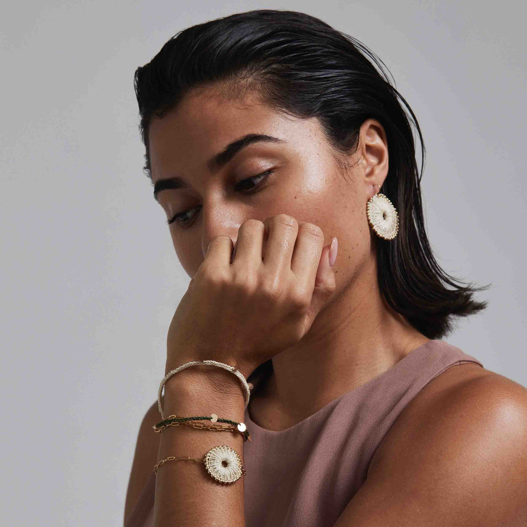 Woman wearing gold earrings and bracelets against a neutral background