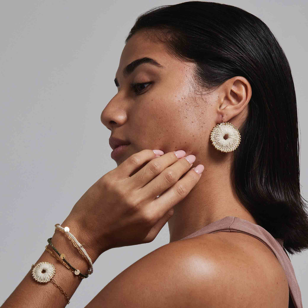 Woman wearing gold earrings and bracelets against a neutral background