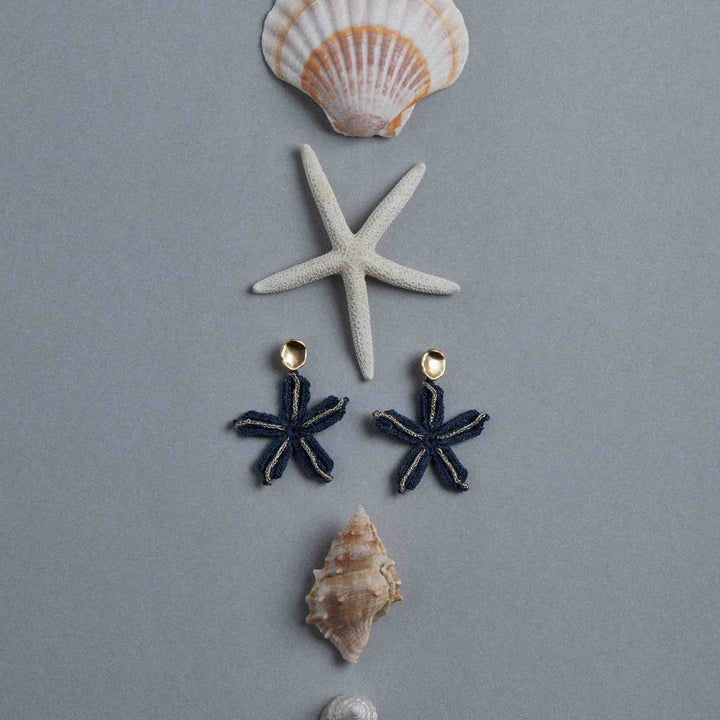 Pair of star-shaped earrings with gold accents on a gray background with shells and a starfish.