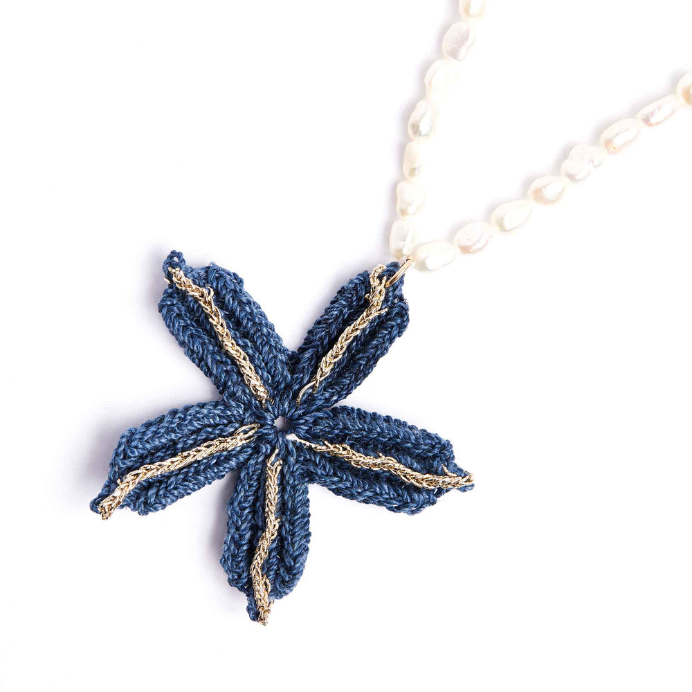 Blue knitted flower pendant on a white chain against a white background