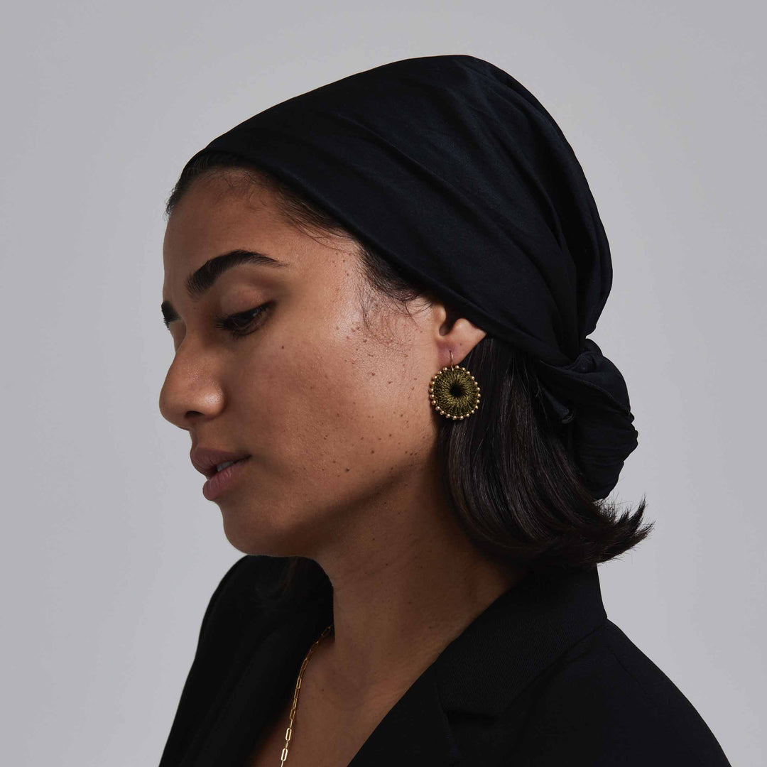 Woman wearing a black headscarf and gold earrings against a gray background