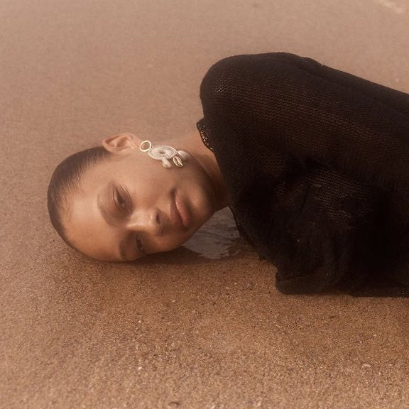 model lying on beach in cowry shell woven earring