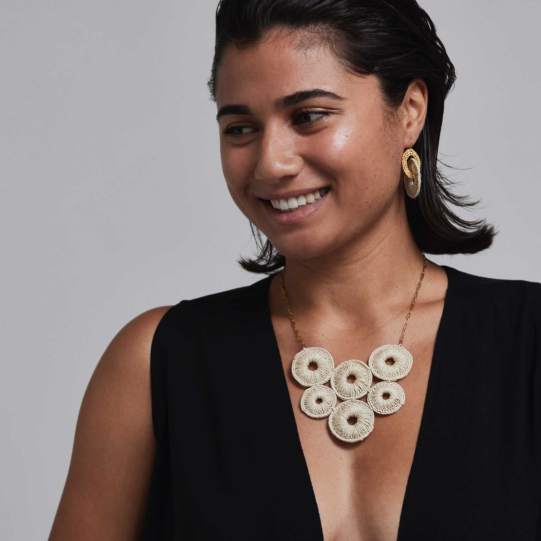 Woman wearing a black top and gold necklace with circular pendants against a gray background